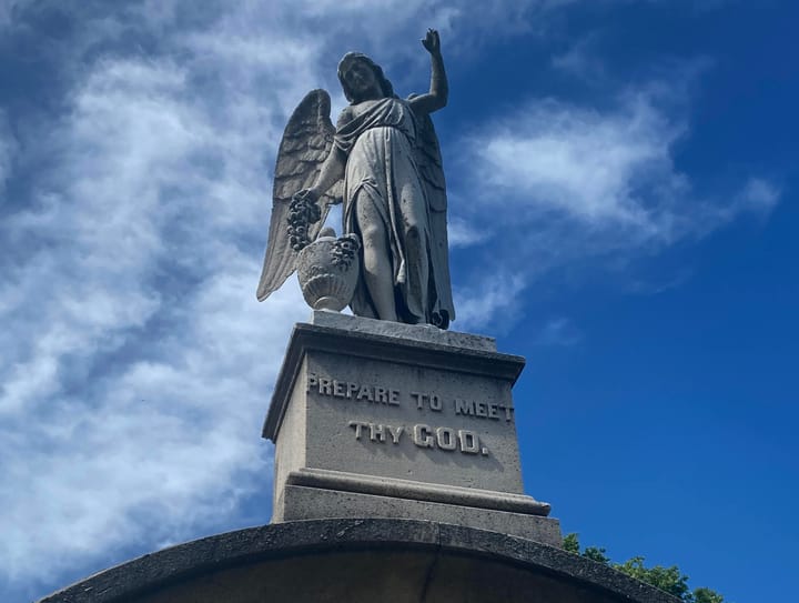 phot of the top of a mausoleum featuring an angel atop a plinth with the inscription "prepare to meet thy god"